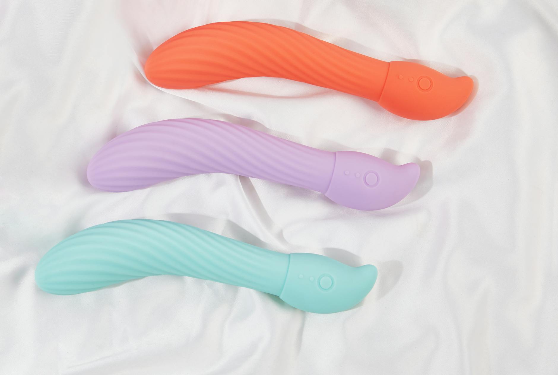 Trois vibrateurs colorés disposés sur un tissu blanc, mettant en évidence leur texture lisse et moderne