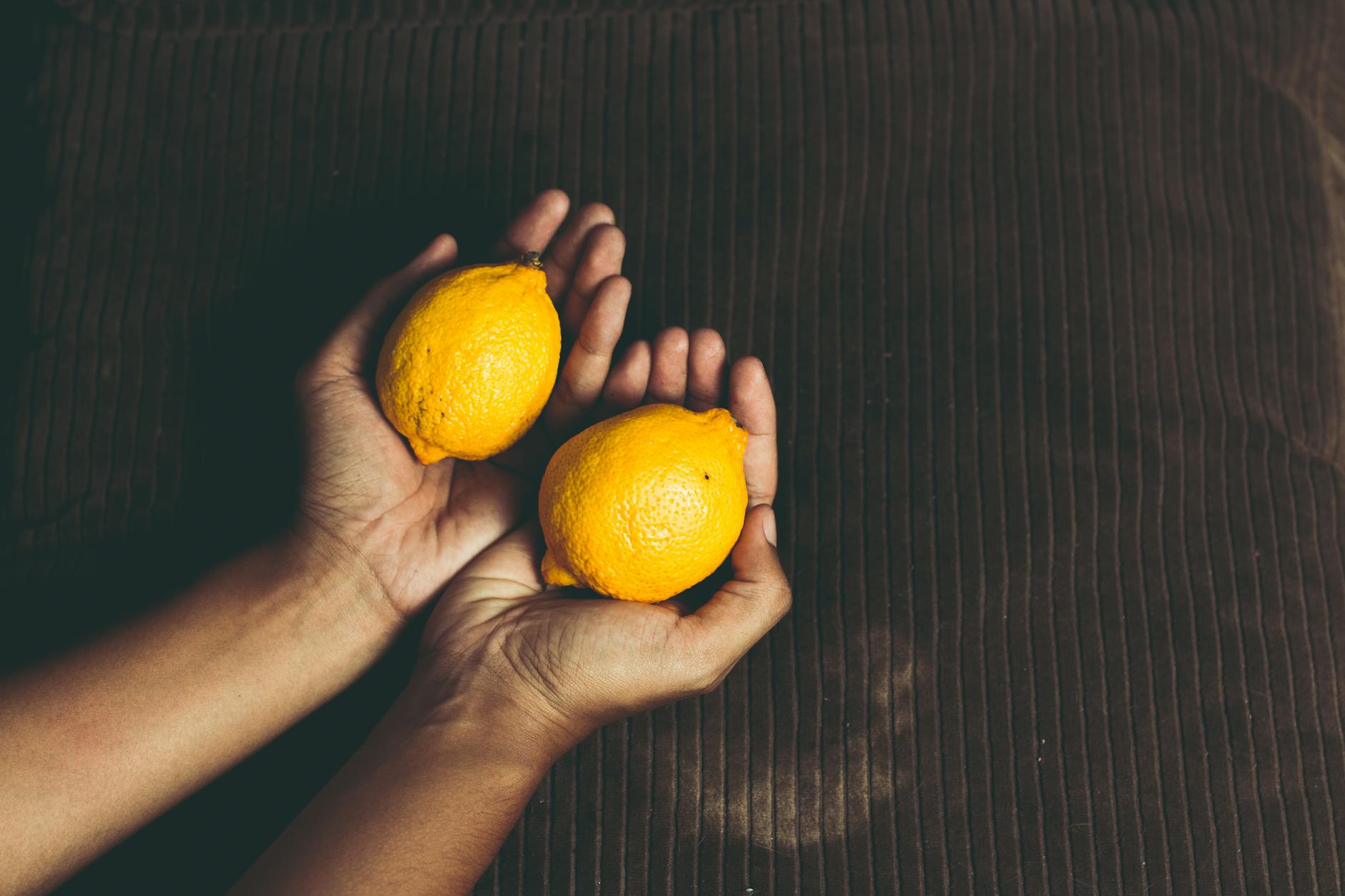 Photo de deux citrons frais dans les mains sur une surface marron
