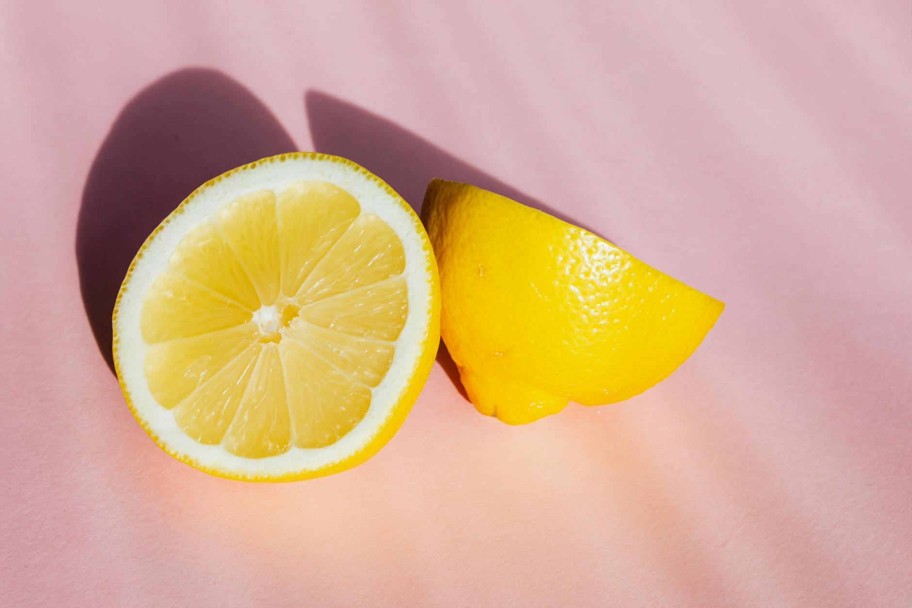 Moitiés de citron frais et juteux disposées sur fond rose dans les rayons du soleil