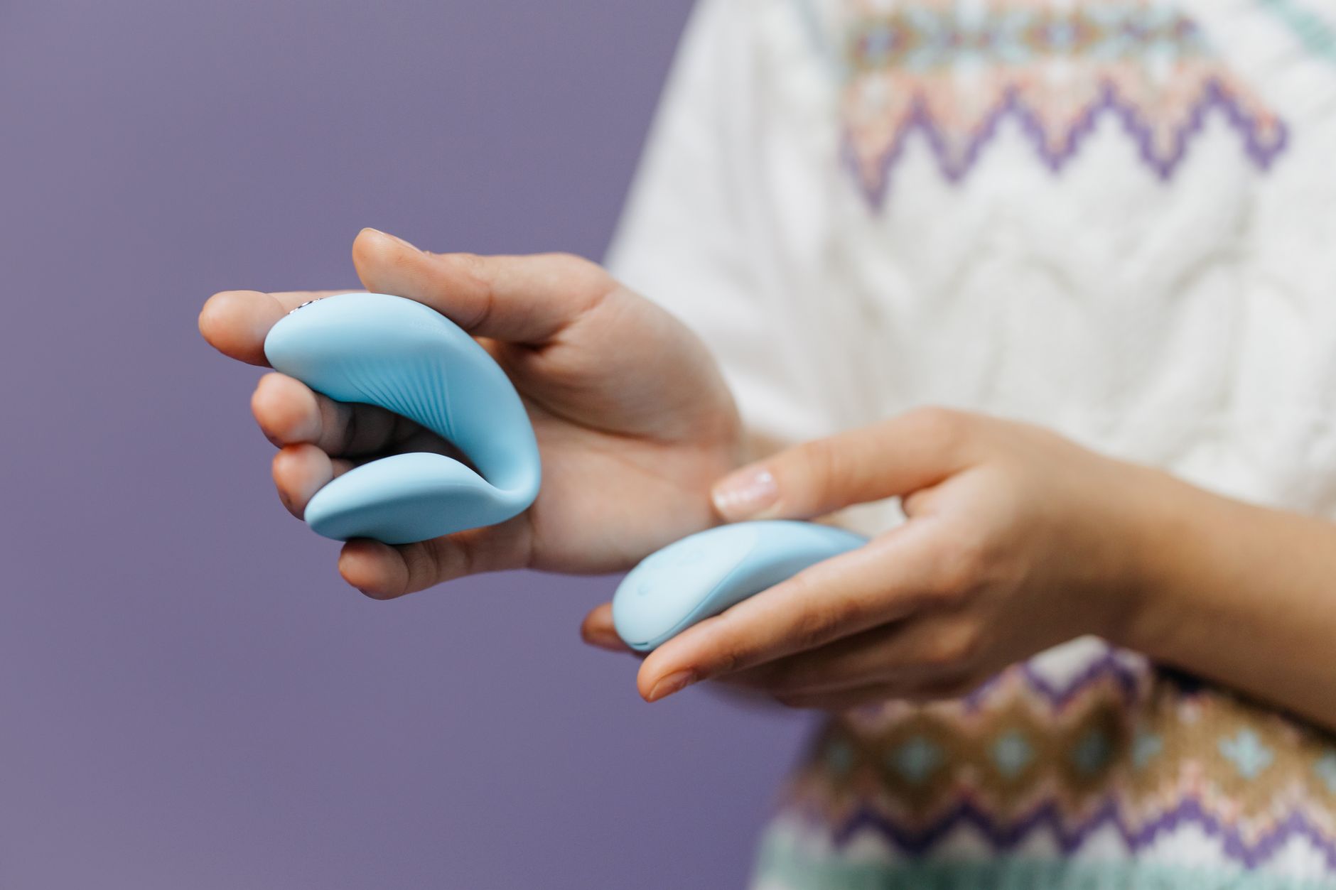 Gros plan des mains tenant un vibrateur bleu élégant contre un fond violet chaleureux