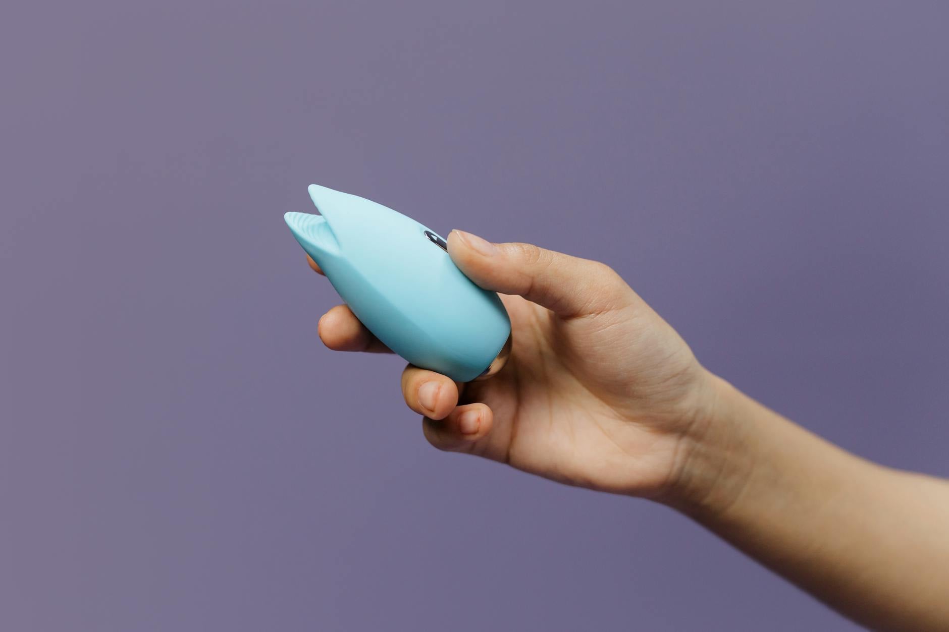 Mains tenant un vibrateur bleu élégant sur fond violet, symbolisant l'exploration personnelle et le plaisir autonome