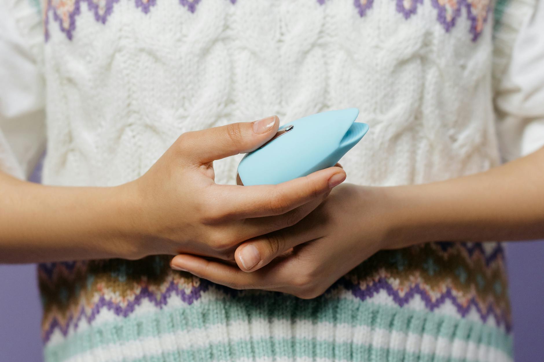 Gros plan des mains tenant un vibrateur bleu contre un pull tricoté doux.