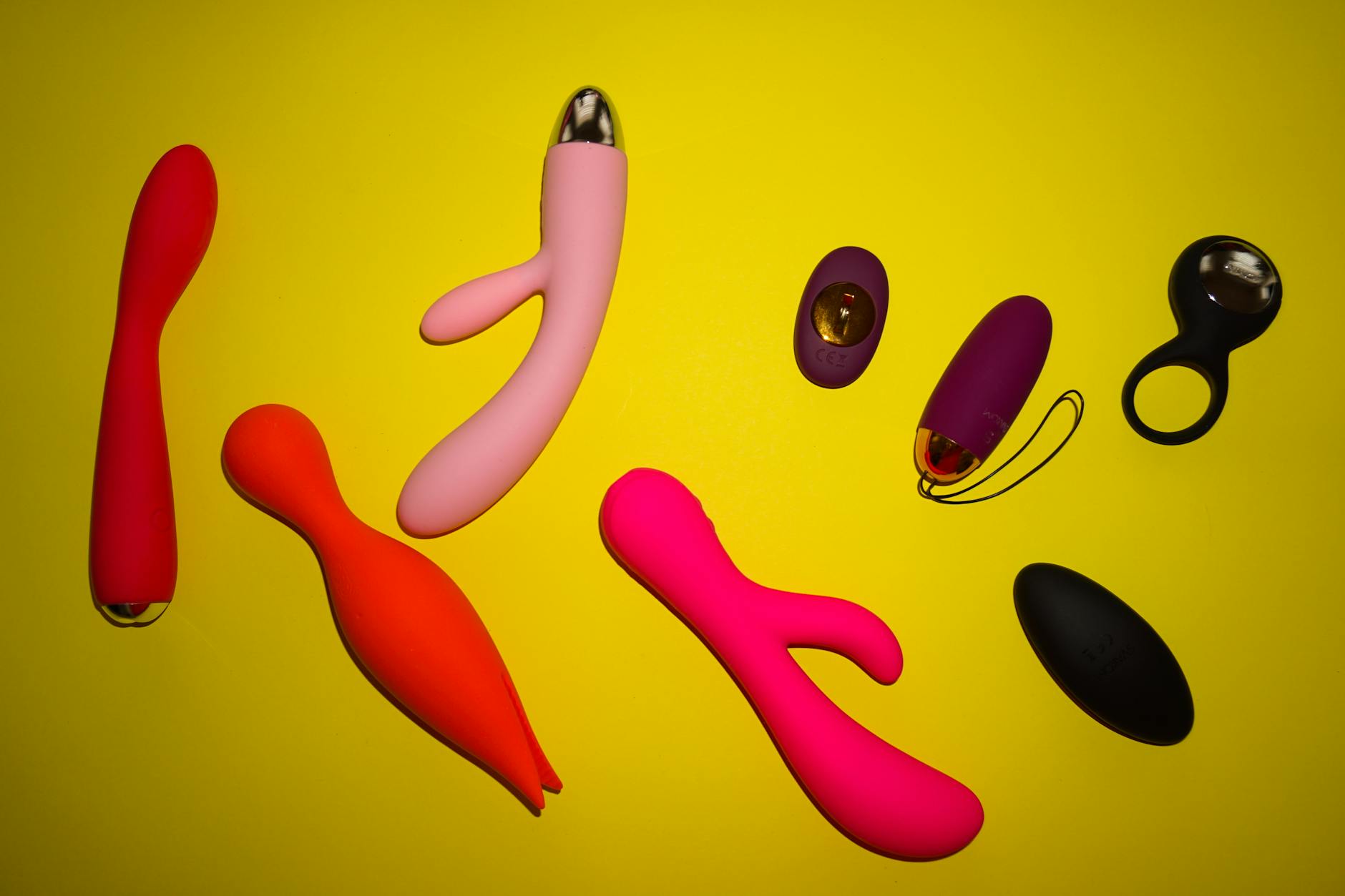 Vibrateurs de différentes couleurs et formes disposés sur une surface jaune vif, représentant la diversité du plaisir